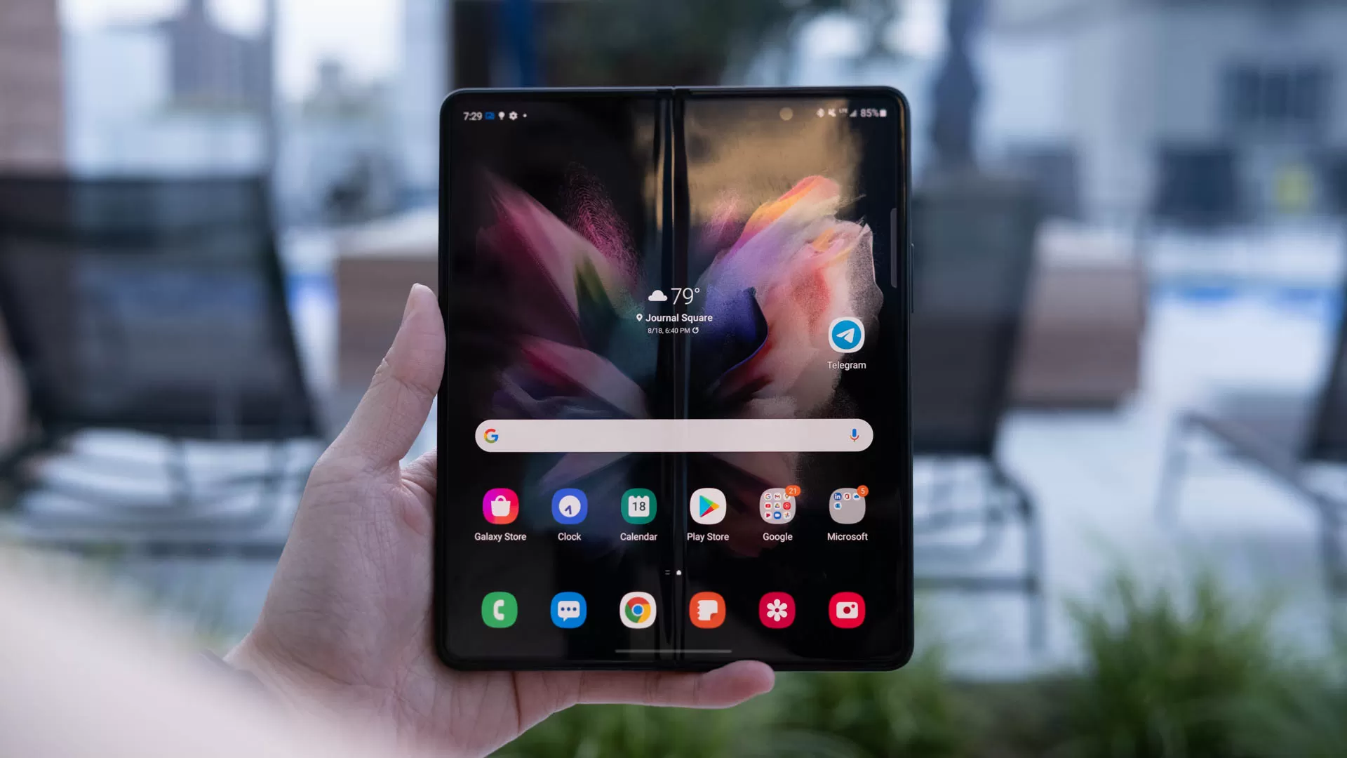 Een hand die de Samsung Galaxy Z Fold 3 omhoog houdt met het scherm open en naar de camera gericht.  Er loopt een vouw in het midden van de startpagina. 